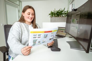 Eine Frau, in der Ausbildung zur Mediengestalterin in Digital und Print, sitzt an einem Schreibtisch mit einem Computer und einem Blatt Papier.
